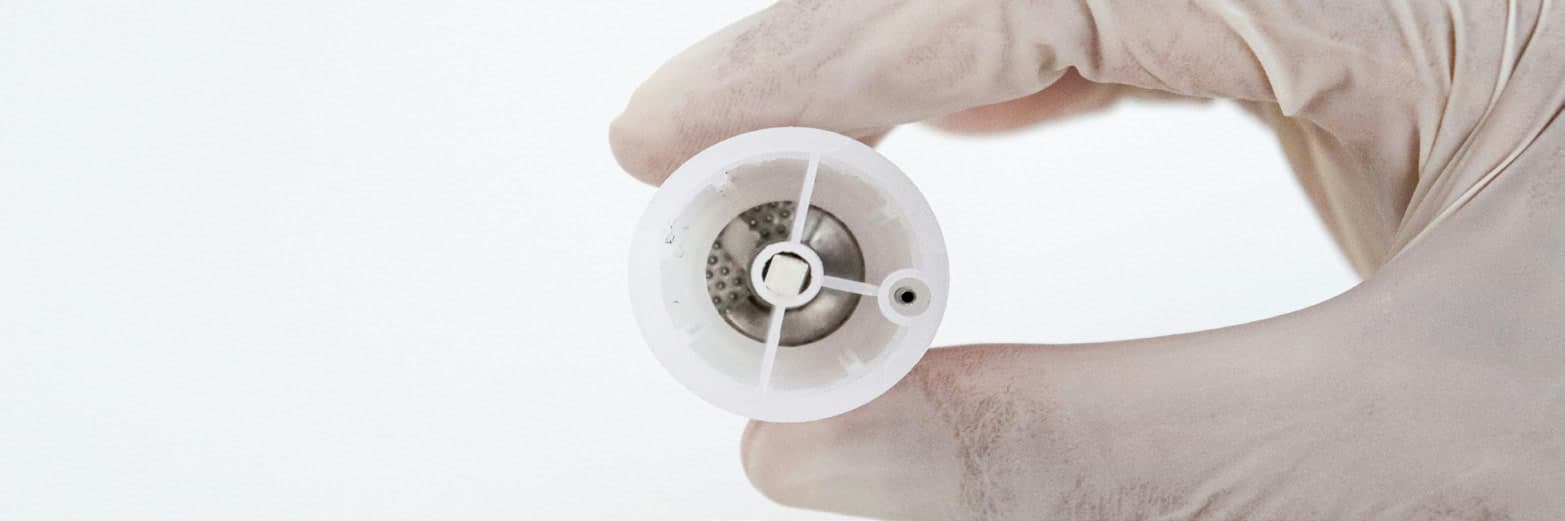 A gloved hand holding the round disaggregation grid of the single-use device.